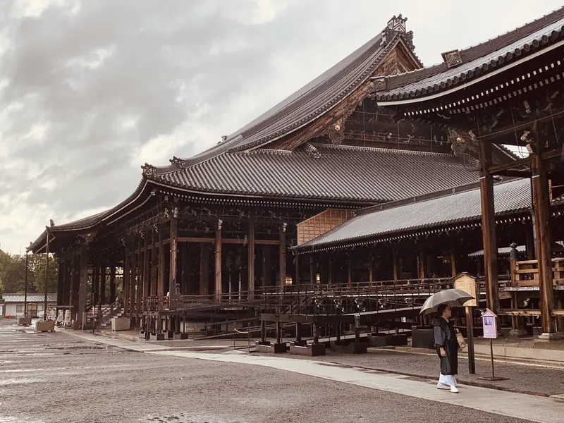 The wooden halls of Nishi Hongan-ji in Kyoto after rain, with one person under an umbrella.